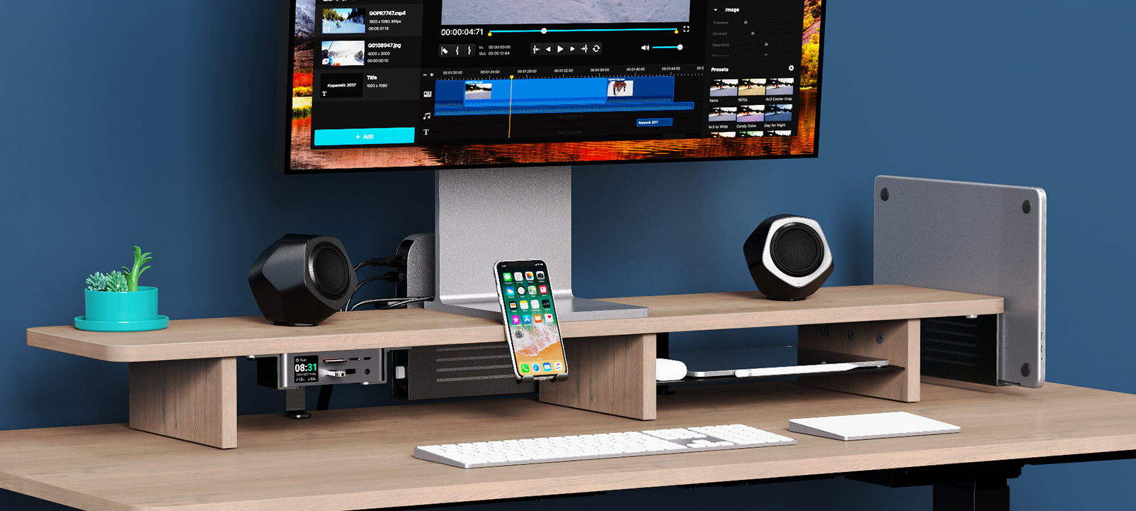 A modern office setup showcasing the éléver Pro Ergonomic Monitor Riser with accessories, including speakers, a phone stand, and a potted plant, highlighting the riser's utility and style.