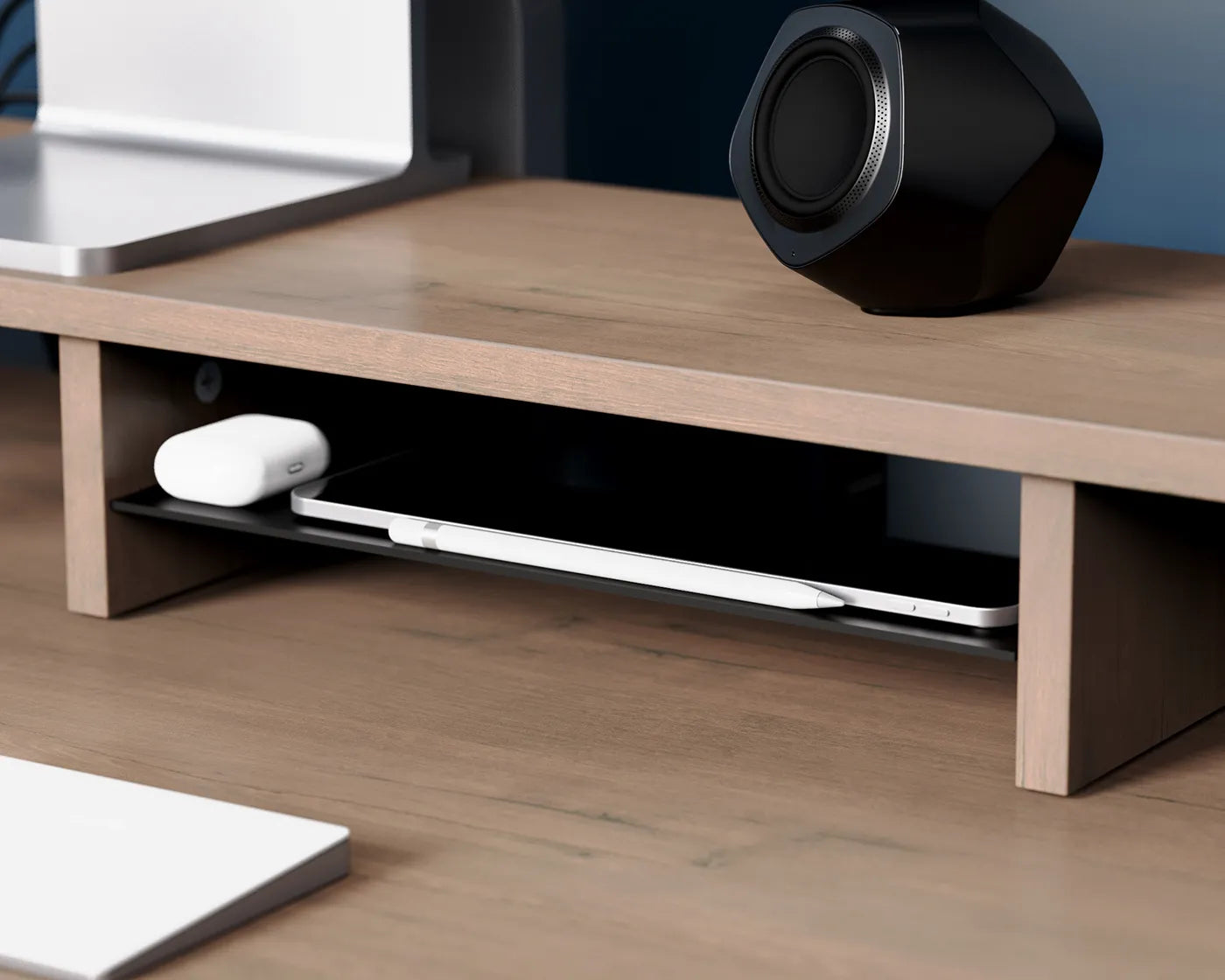 A speaker and a laptop shelf beneath a monitor riser, showcasing the riser's capacity for organizing and streamlining workspaces.