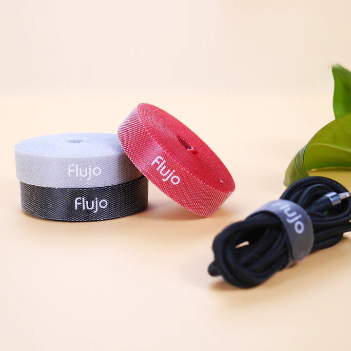 Three Flujo branded velcro cable management straps in white, black, and red colors, coiled next to a neatly bundled cable, on a light beige surface