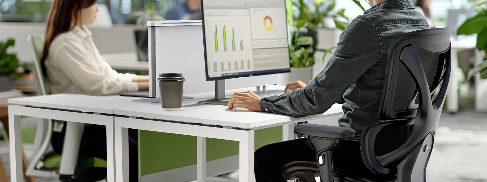 Two professionals working in a modern office equipped with ergonomic furniture. The focus is on a man sitting in a comfortable ergonomic chair, facing dual monitors displaying charts and data. The text overlay reads, "Customize. Optimize. Maximize Productivity."