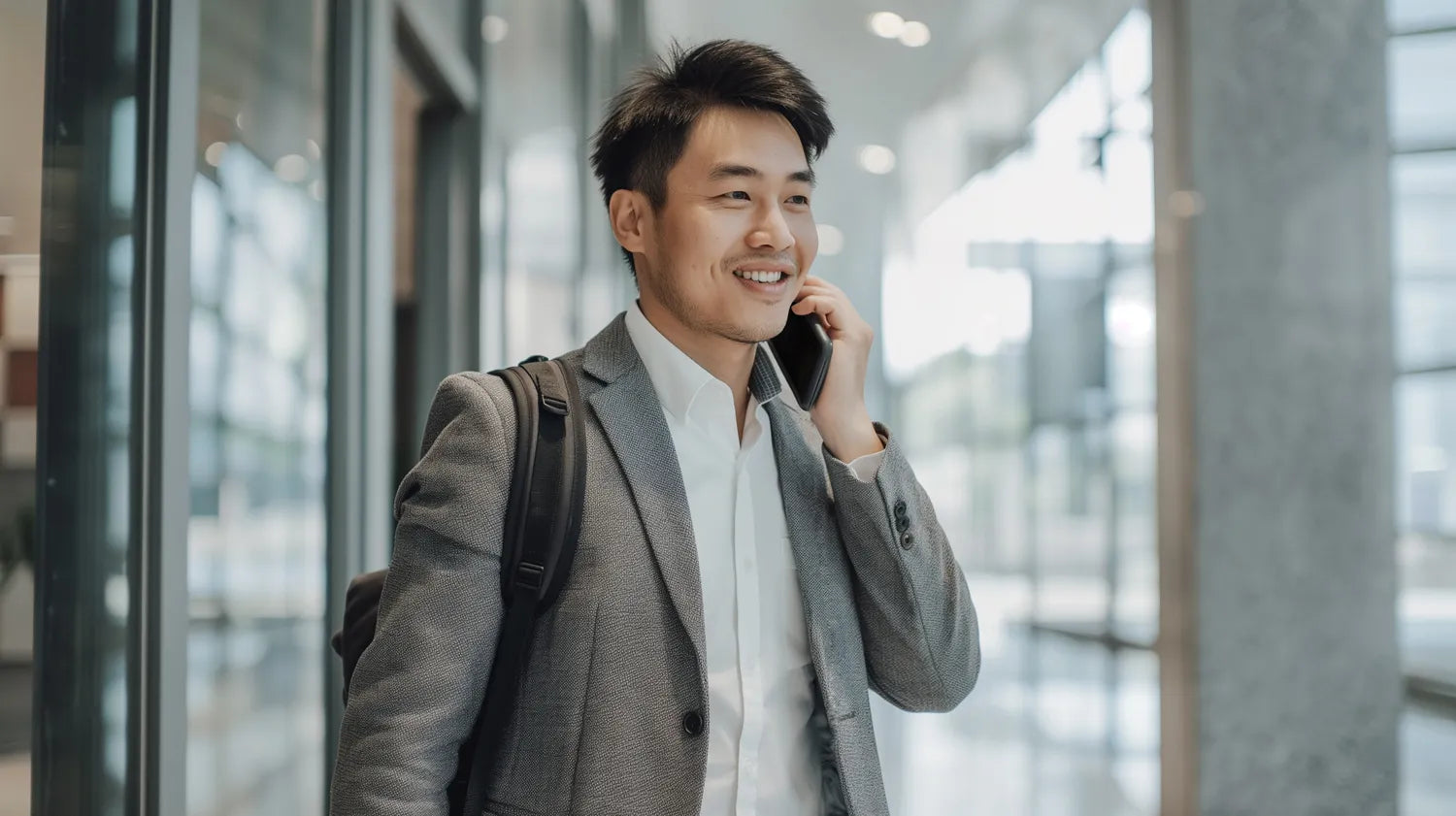 Business professional making a phone call in a modern office setting, carrying a backpack and wearing a suit, smiling while walking