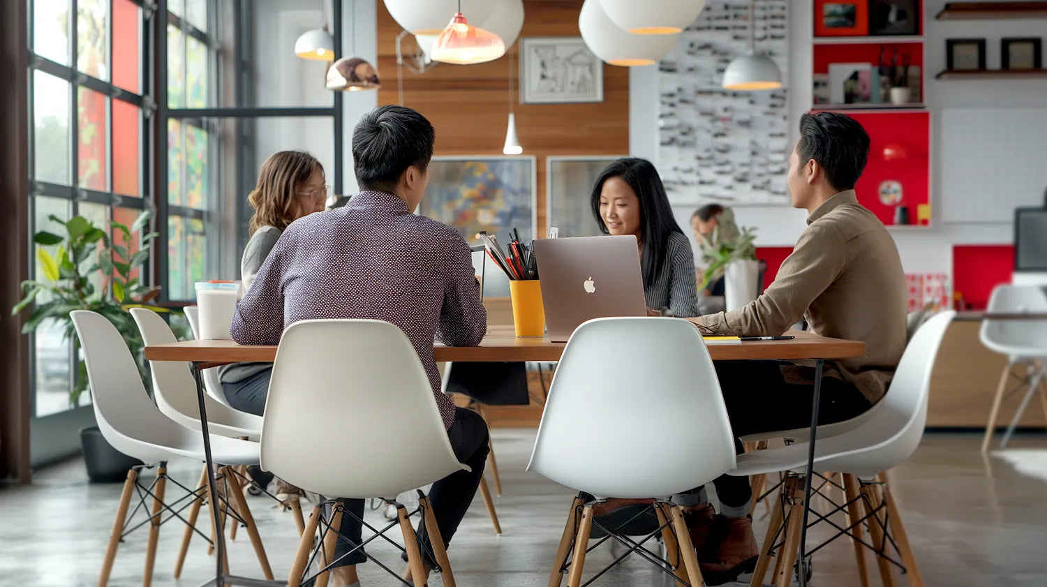 Team collaborating in a modern office workspace, engaging in a meeting around a shared table with laptops and notebooks